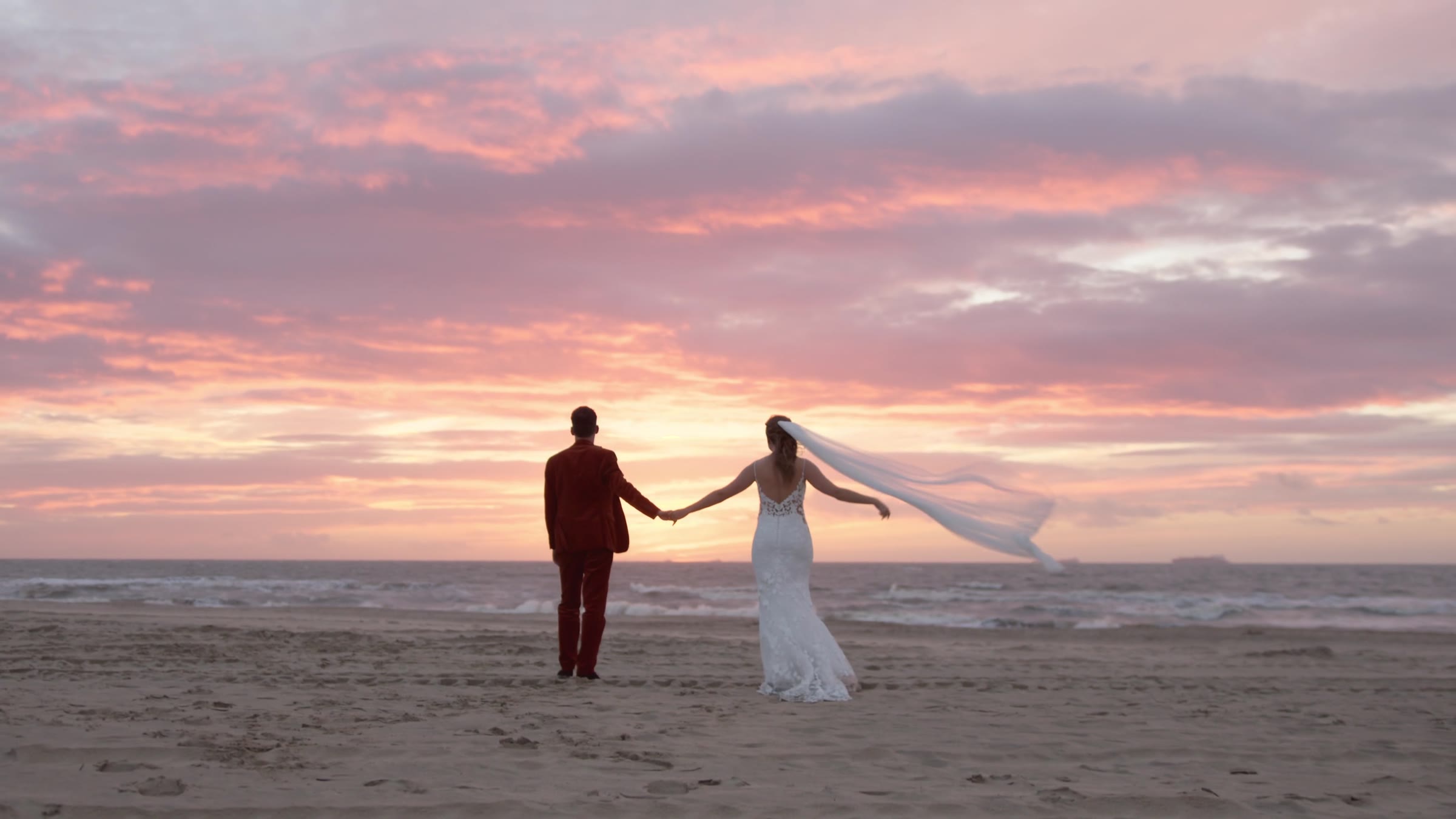 Bruidspaar hand in hand op het strand bij zonsondergang